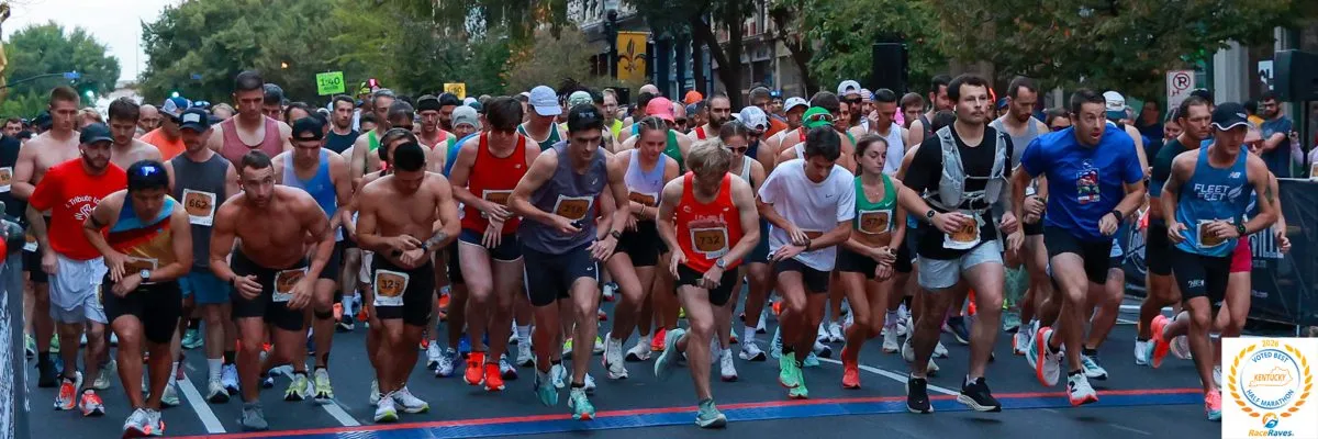 A large group of runners at the starting line of an urban half marathon, with many participants in motion.