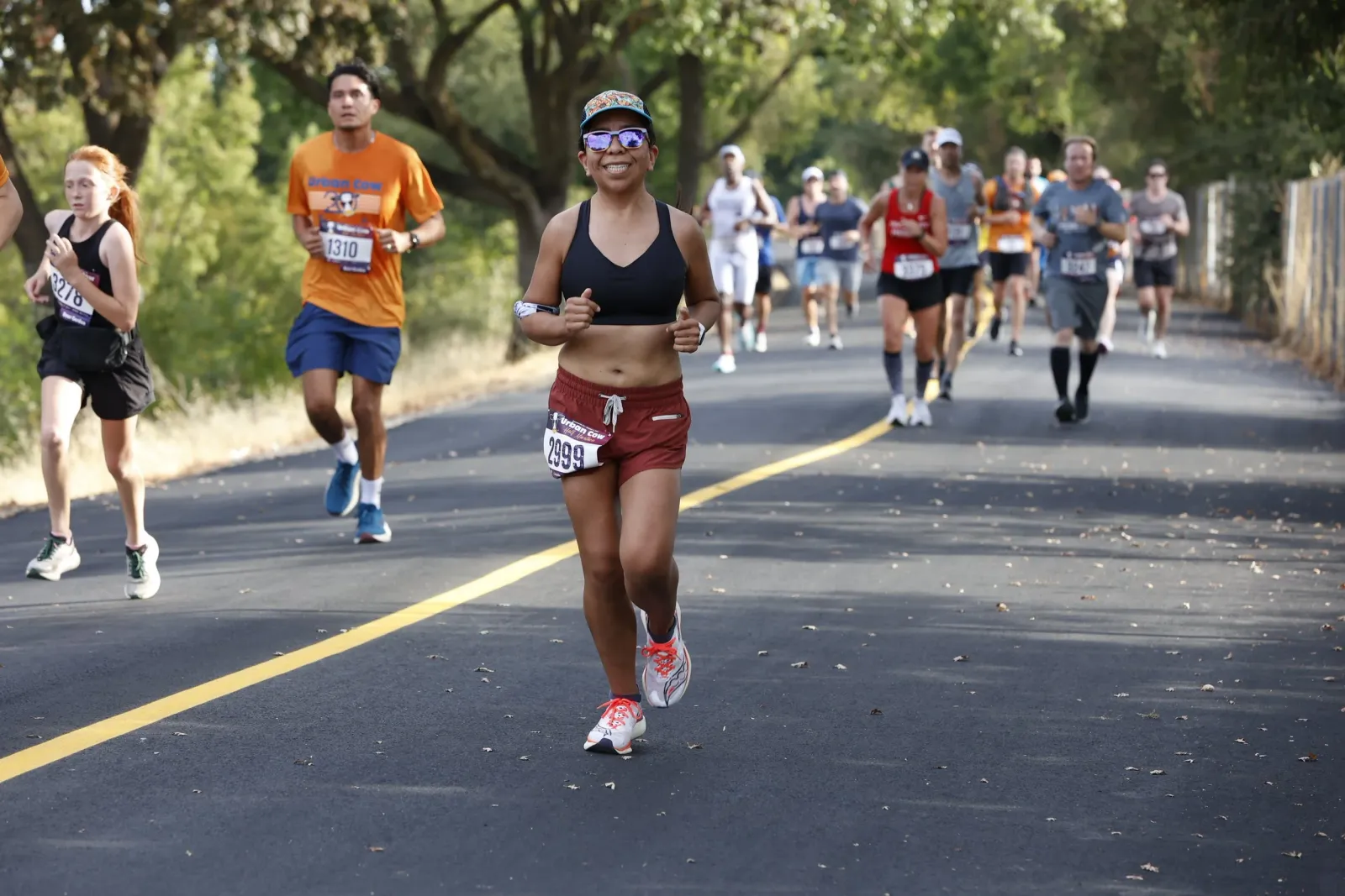 Runners participating in the Urban Cow Half Marathon, with a woman in the foreground smiling and giving a thumbs up.