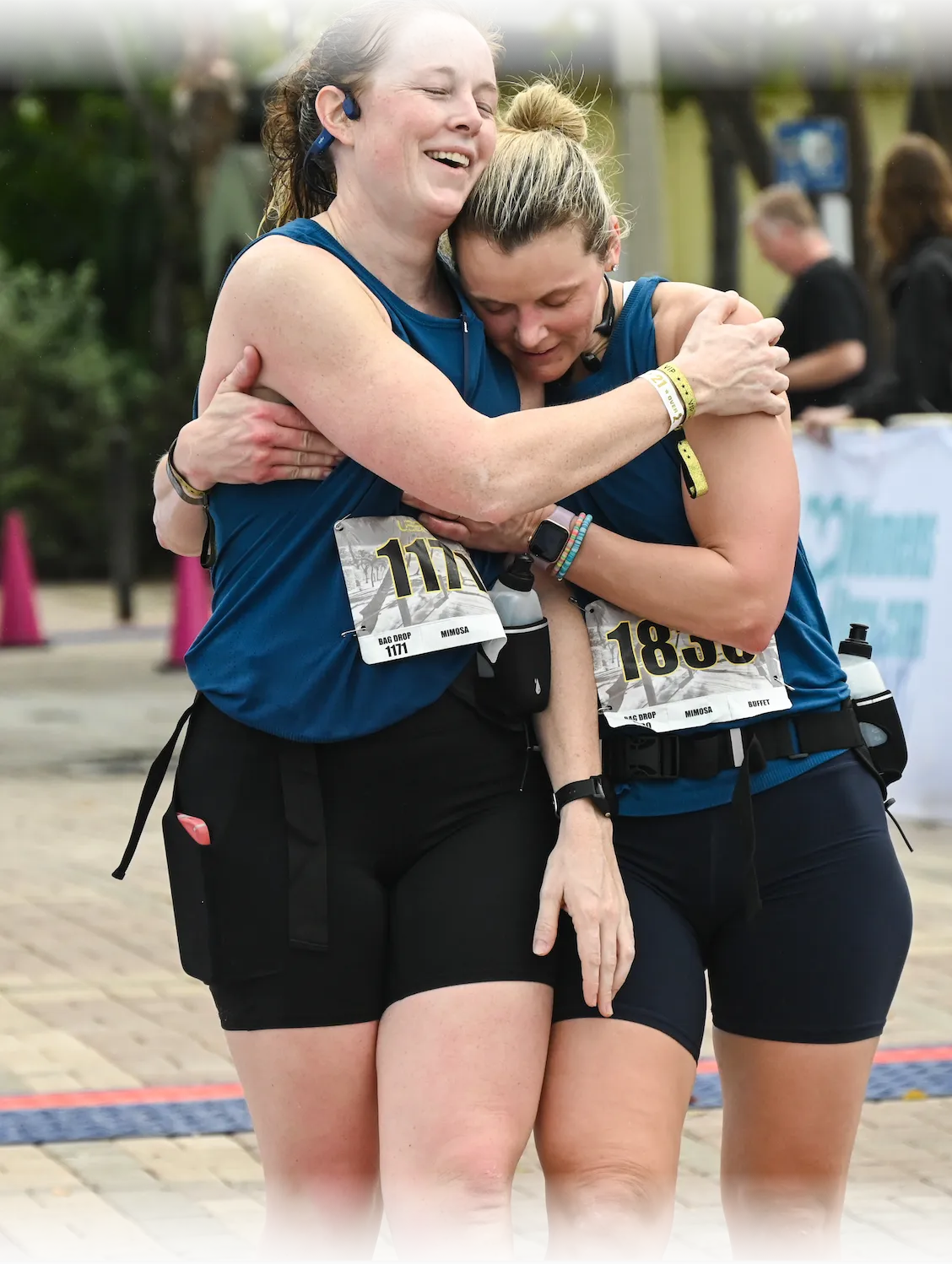 Two female runners embracing and celebrating at the finish line of a race.