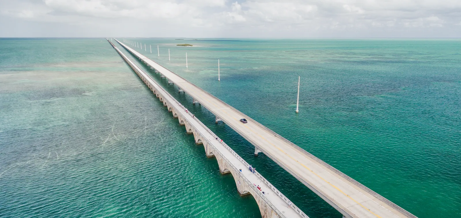 A long bridge over turquoise water, with a few runners visible on the pedestrian walkway.