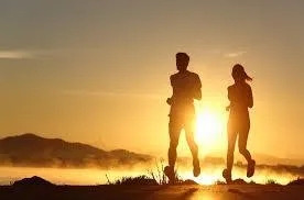 Two runners silhouetted against a vibrant sunrise, with mountains in the background.