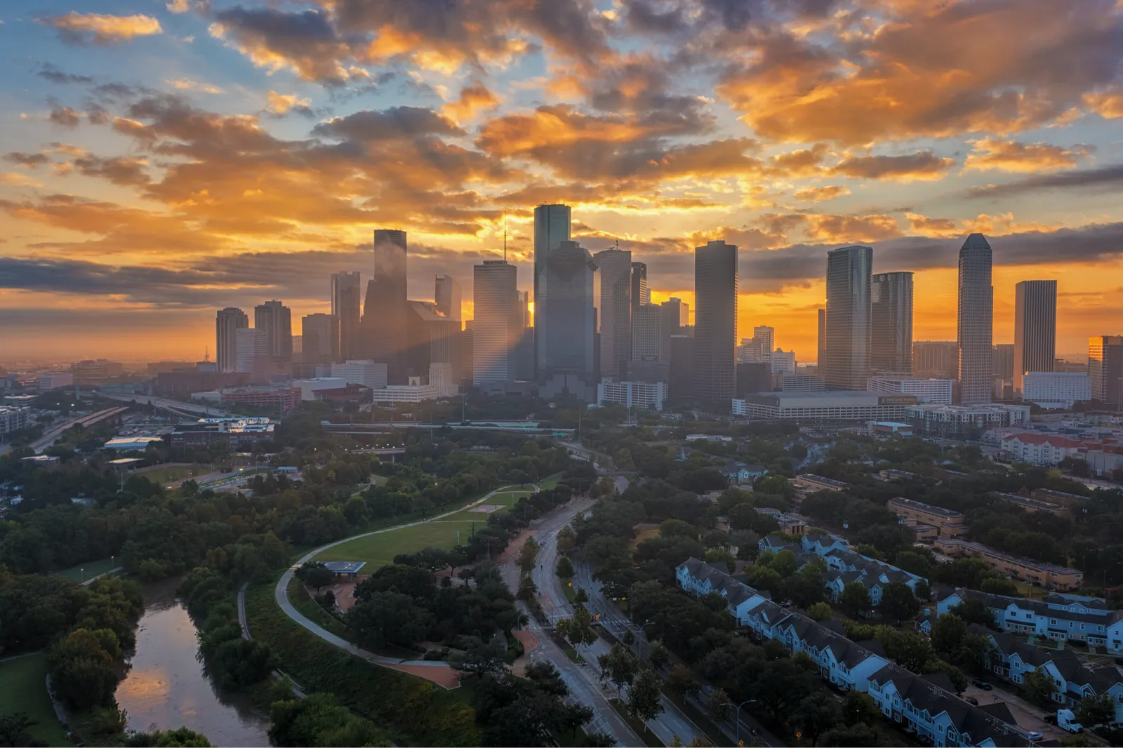 Houston skyline at sunrise with a river and park in the foreground.
