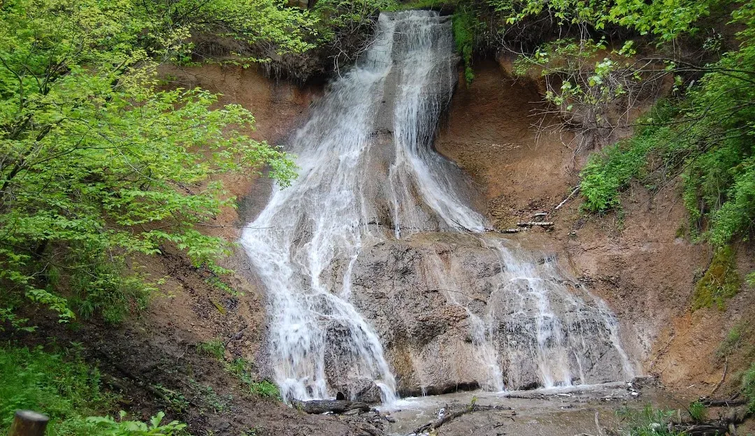 A picturesque waterfall cascading down a rocky cliff face surrounded by lush green foliage.