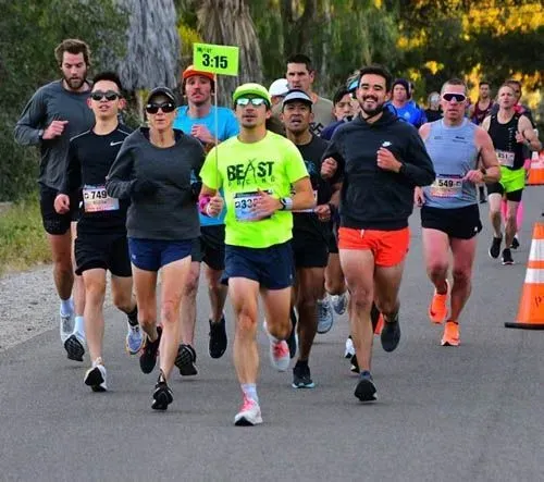 A group of runners in the foreground, with more runners in the background, on a paved road during a race.