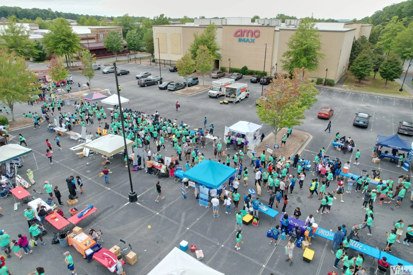 Aerial view of a large crowd of runners and volunteers gathered in a parking lot before a race, with tents and tables set up.