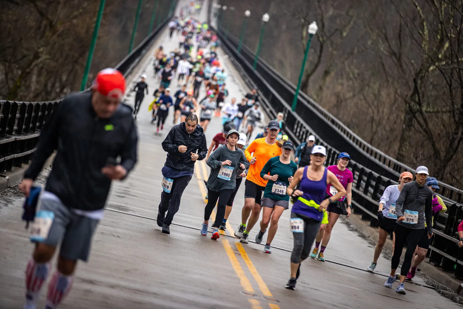 Runners crossing a bridge during a race on a cloudy day.