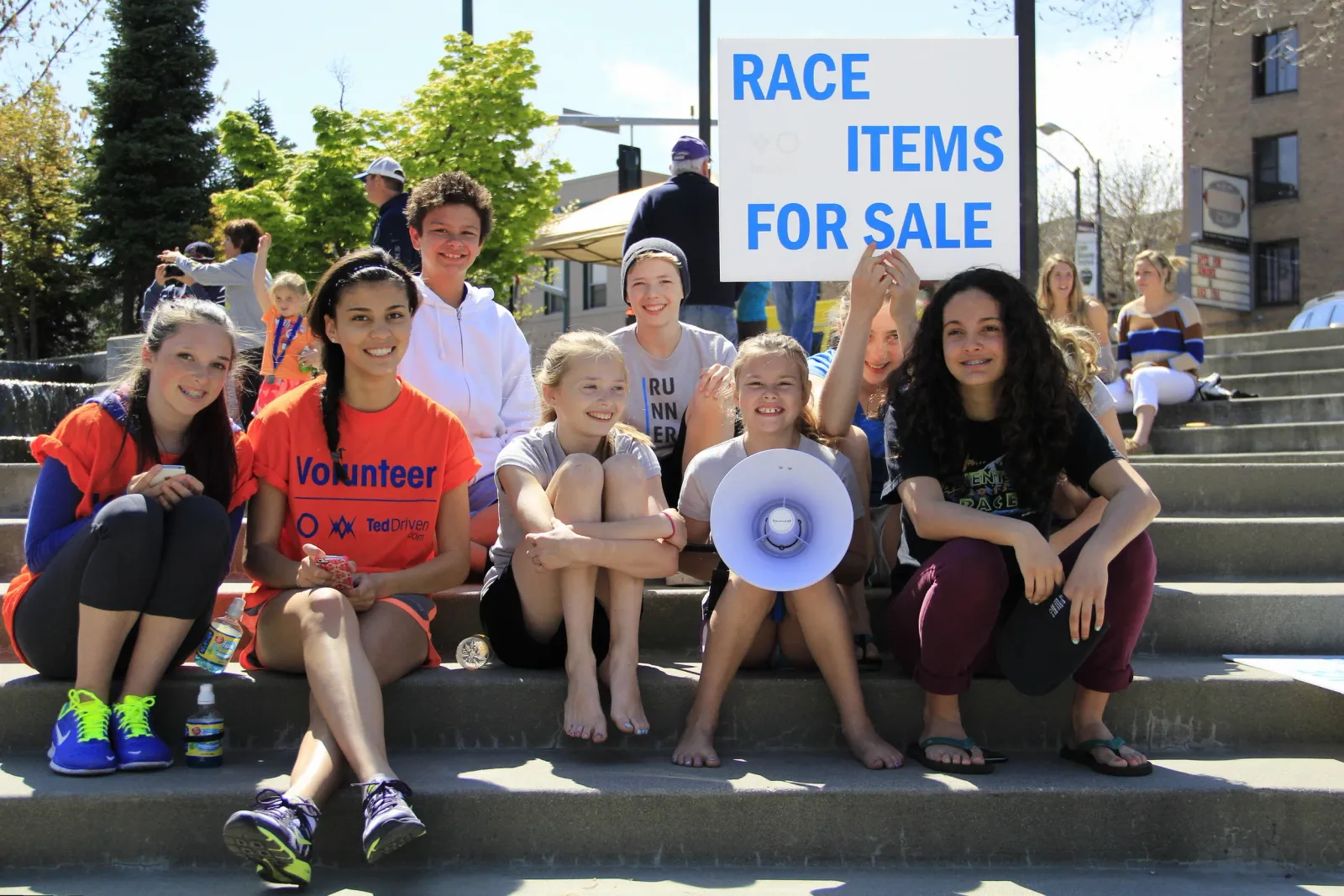 A group of young people, some wearing race t-shirts, sitting on steps and smiling.