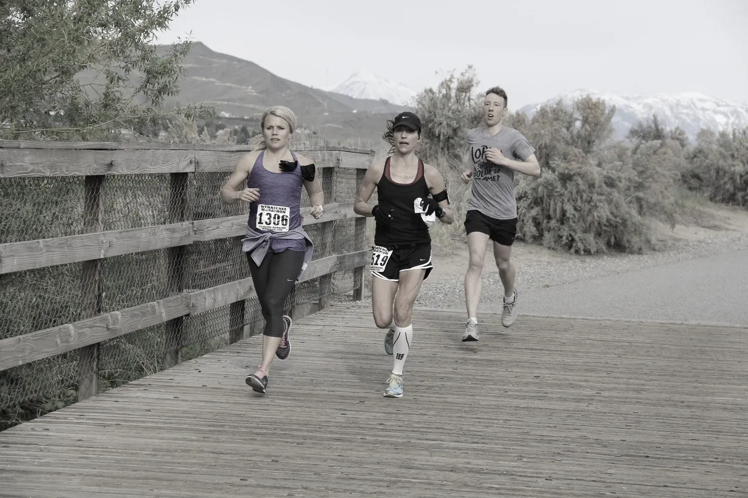Three runners on a wooden bridge with mountains in the background during the Wenatchee Marathon.