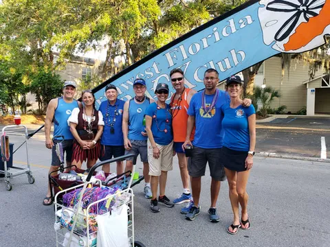 A group of runners, some wearing medals, pose in front of a blue banner that reads 'Northwest Florida Track Club'.