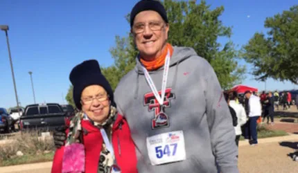 Two people, an older man and woman, smiling at the camera, wearing race bibs and medals.