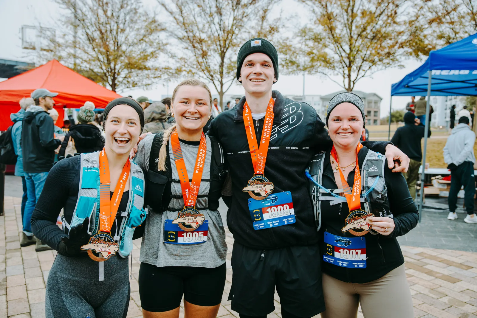 Four smiling runners pose for a photo, proudly displaying their Wilmington Historic Half Marathon medals.
