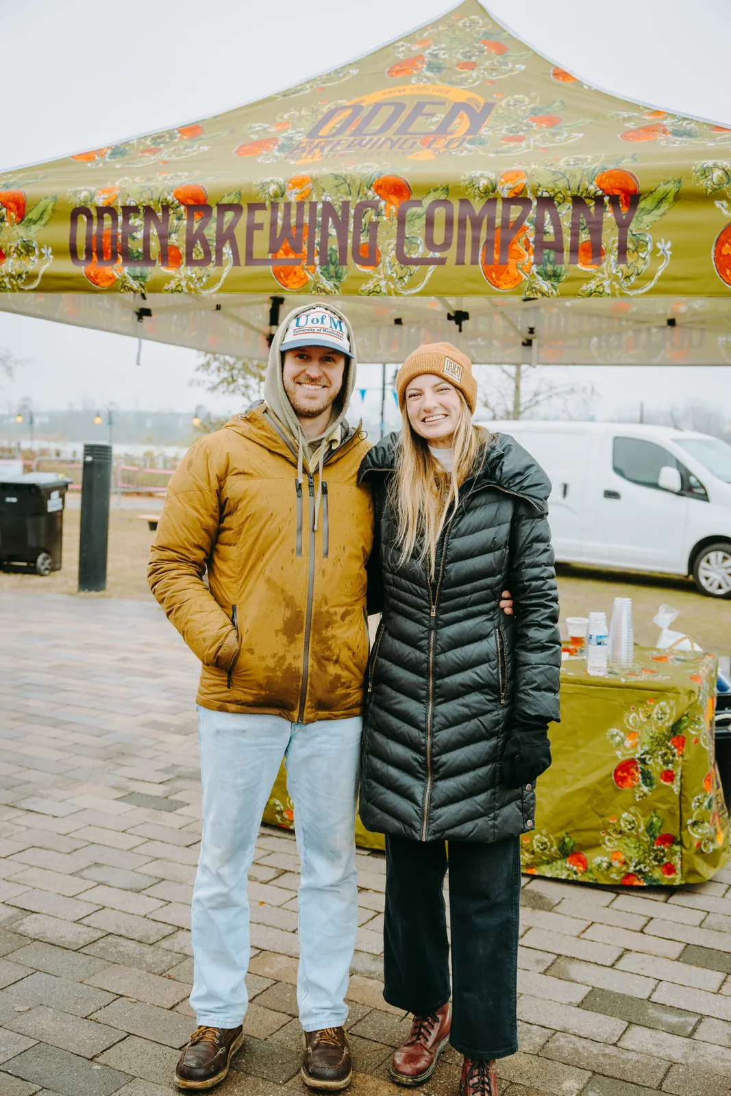 A smiling couple stands in front of a tent at an outdoor event.