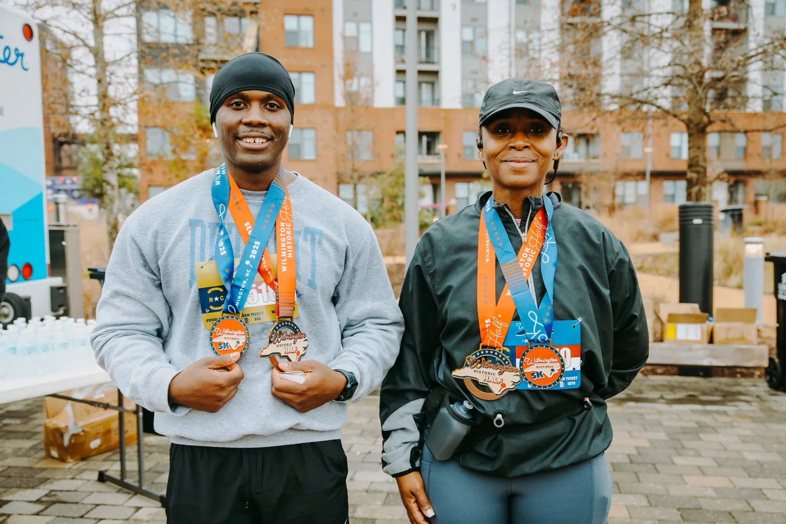 Two smiling runners, a man and a woman, proudly display their Wilmington Historic Half Marathon and 5K medals.