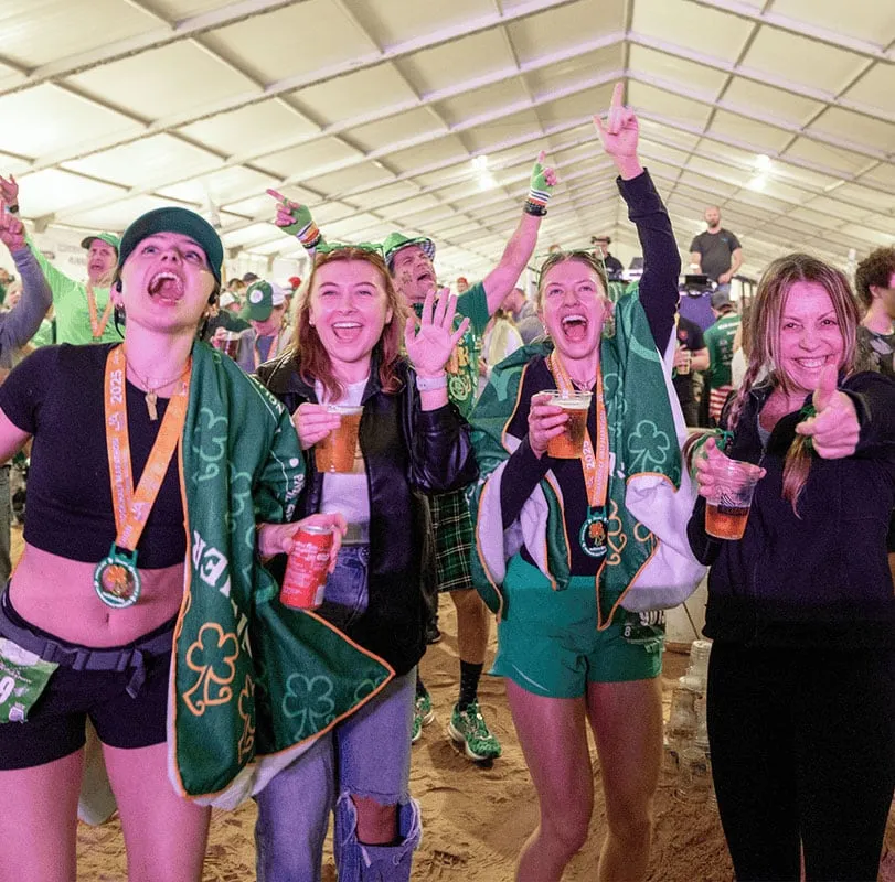 A group of women celebrating at a race event, wearing medals and holding drinks.
