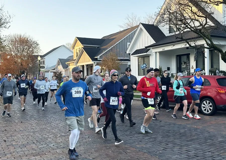 Runners participating in a race on a brick road with houses in the background.