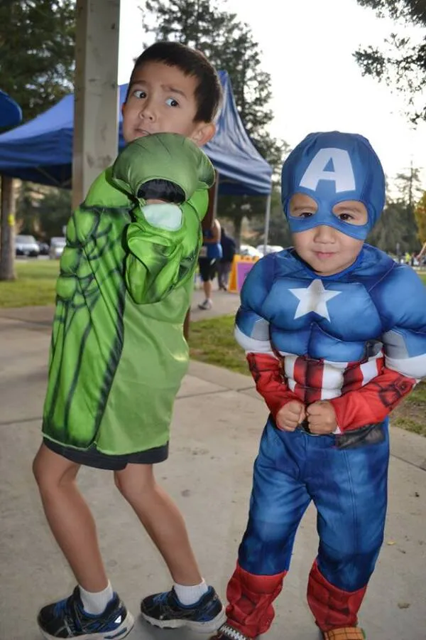 Two children in superhero costumes, one as Captain America and the other as the Hulk, posing for a photo.