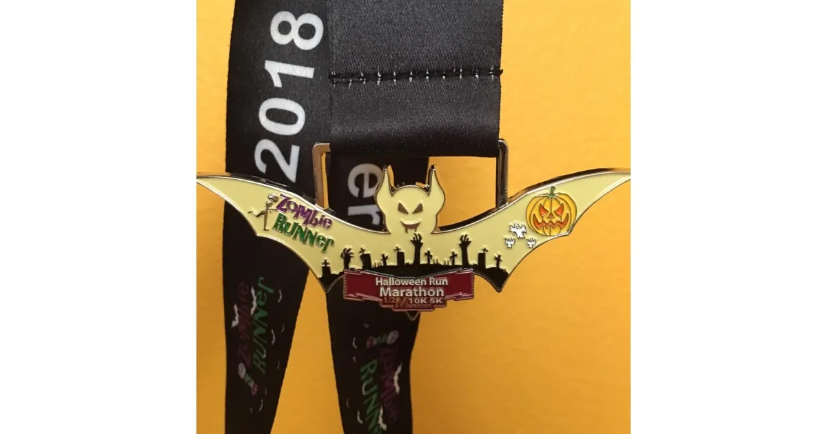 Halloween Run Marathon medal shaped like a bat with a pumpkin and zombie runner graphic.