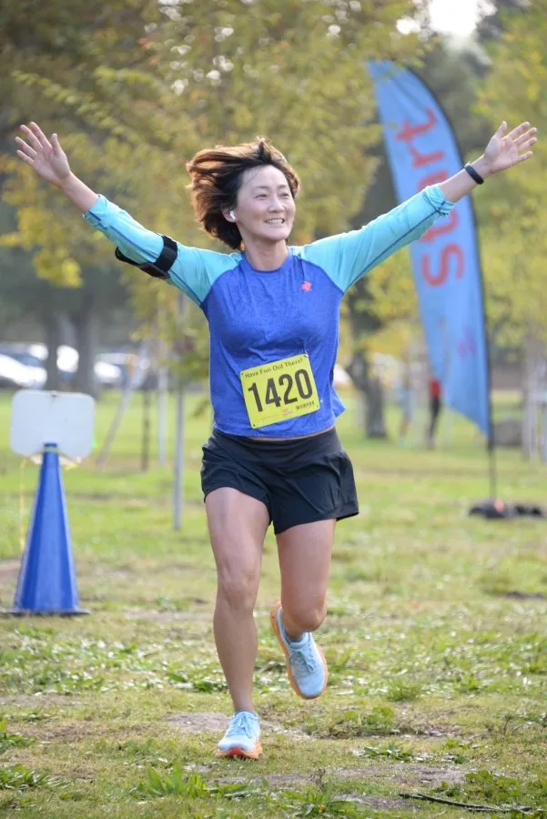 A female runner with her arms raised in celebration crosses the finish line, wearing bib number 1420.