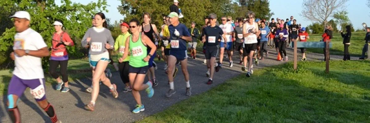 A group of runners on a paved path surrounded by grass and trees.