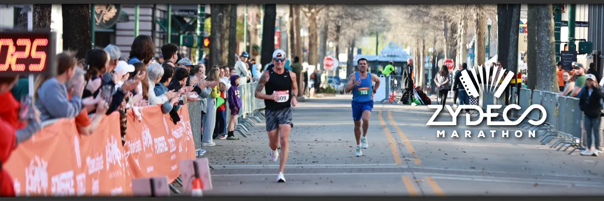 Runners race down a city street lined with cheering spectators, with the Zydeco Marathon logo visible.